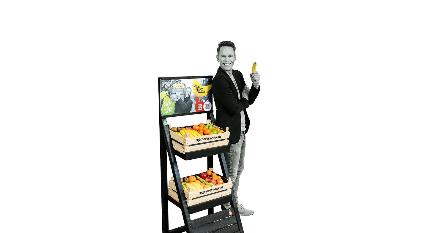 man kijkt blij, heeft een banaan in zijn hand en staat bij de display voor fruit op je werk